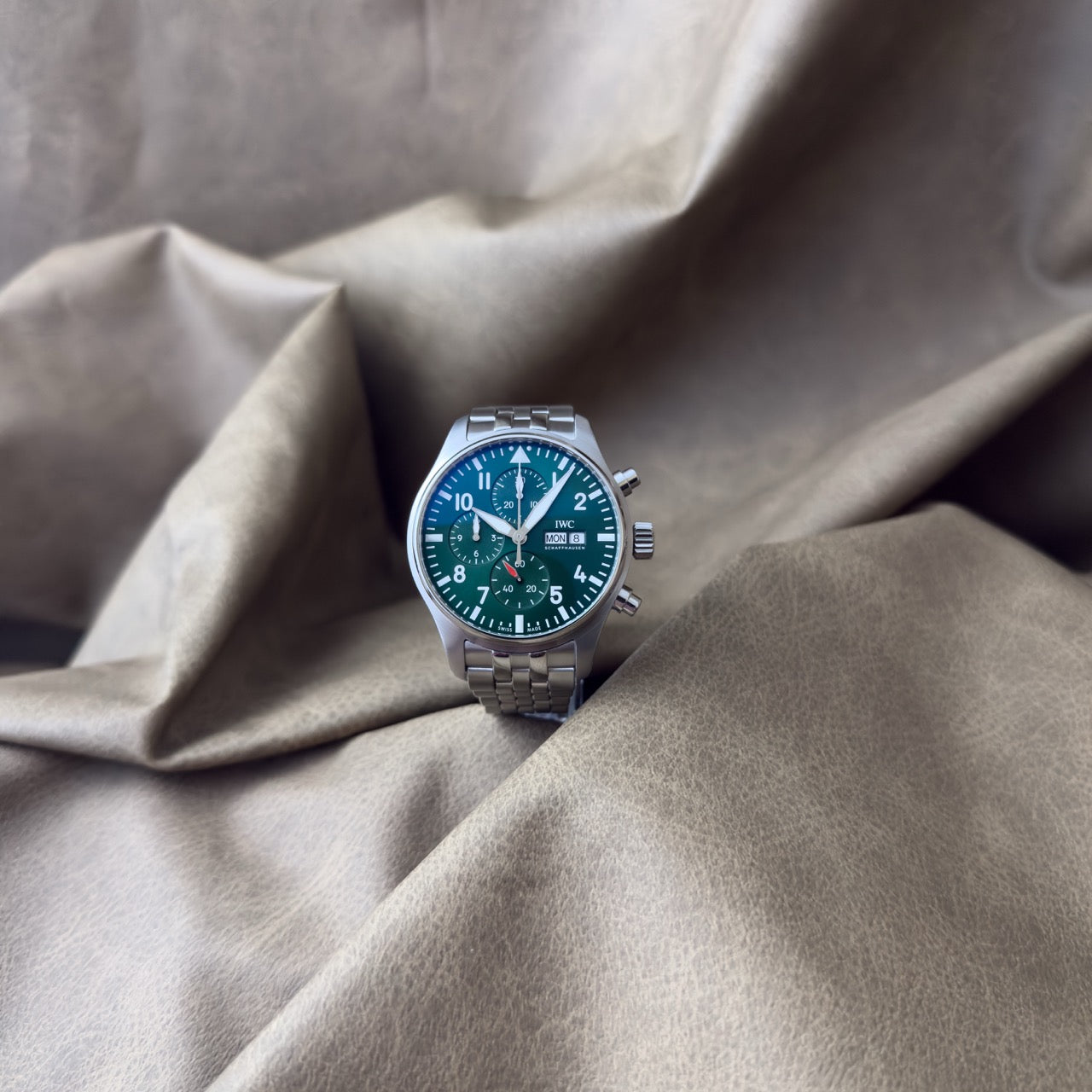 Watch with a green face and silver case on a textured beige fabric background